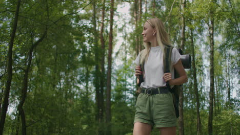Slow-motion-portrait:-Adult-caucasian-blonde-woman-wearing-shorts-and-t-shirt-hikes-through-woods.-Young-lady-hiking